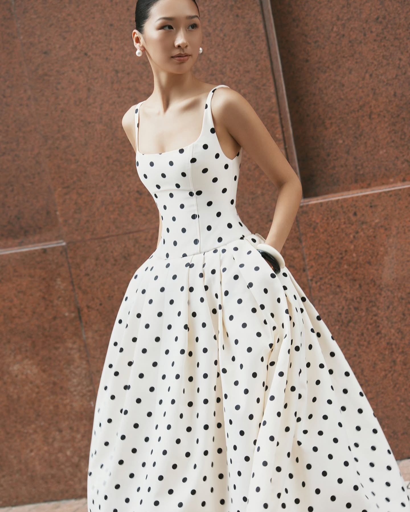 A stylish woman wearing an old money style polka dot dress, standing gracefully in a hotel, showcasing the dress’s classic silhouette and timeless elegance