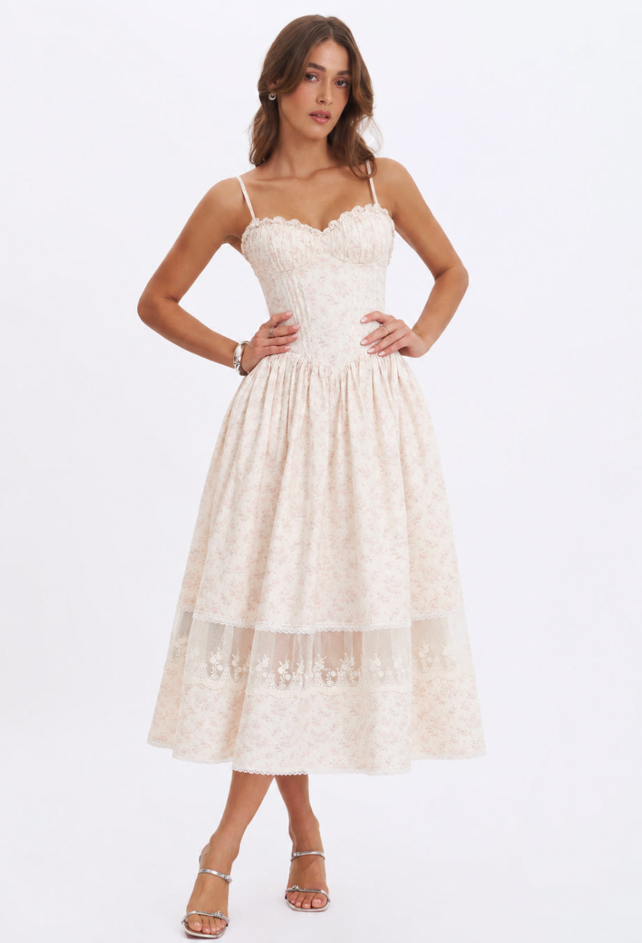 A woman in a white floral formal dress, posing elegantly on the beach, wearing a piece from Deesse Blanche Fashion Canada.