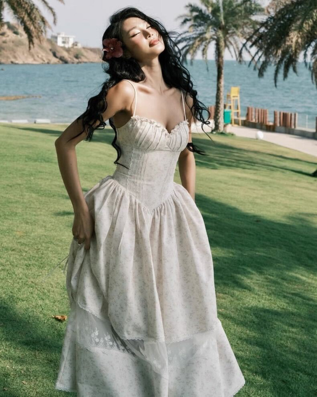 A woman in a white floral formal dress, posing elegantly on the beach, wearing a piece from Deesse Blanche Fashion Canada.